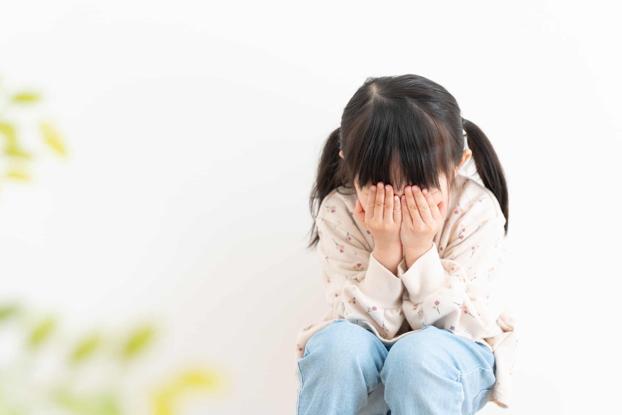 悪い歯並びが恥ずかしくて顔を隠してうずくまる子ども